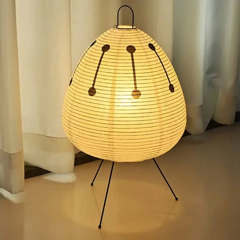 Modern egg-shaped paper floor lamp with black tripod legs and decorative black dots emitting warm yellow light