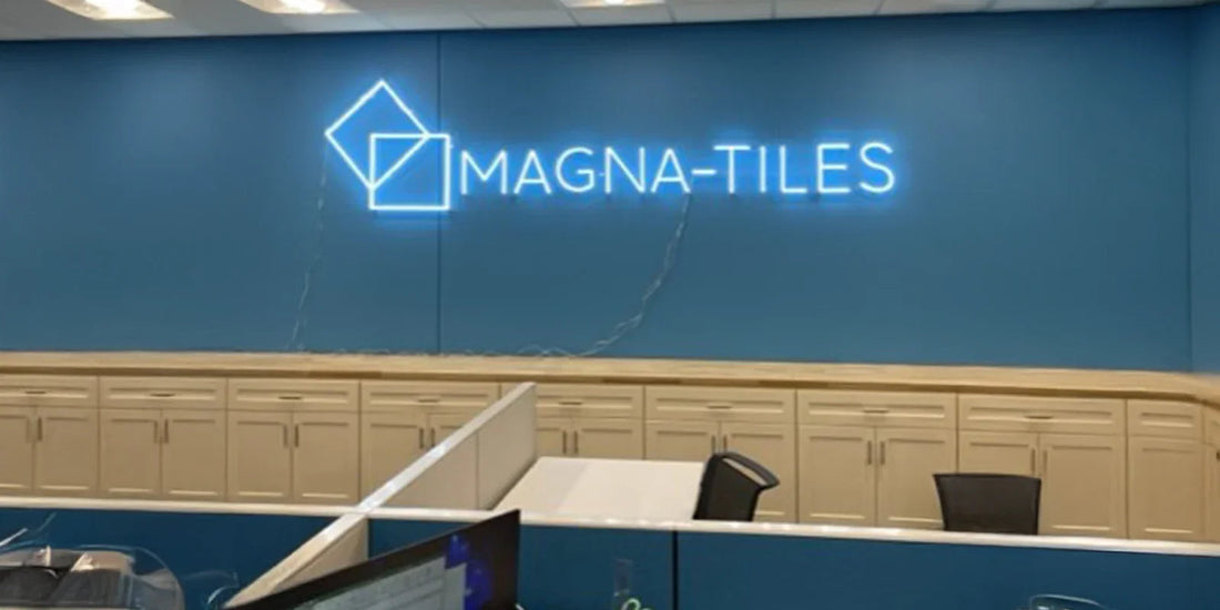 Modern office workspace with blue wall featuring illuminated Magna-Tiles logo and light wood cabinets