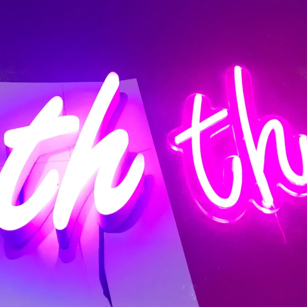Close-up of bright pink and purple neon signs spelling the letters 'th' in cursive script on dark and light backgrounds