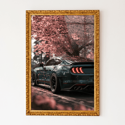 Framed canvas wall art in an ornate gold frame featuring a sleek dark sports coupe parked beneath blooming pink cherry blossom trees.