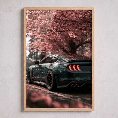 Oak framed canvas print featuring a dark green modern sports car parked beneath blooming cherry blossom trees with falling pink petals.