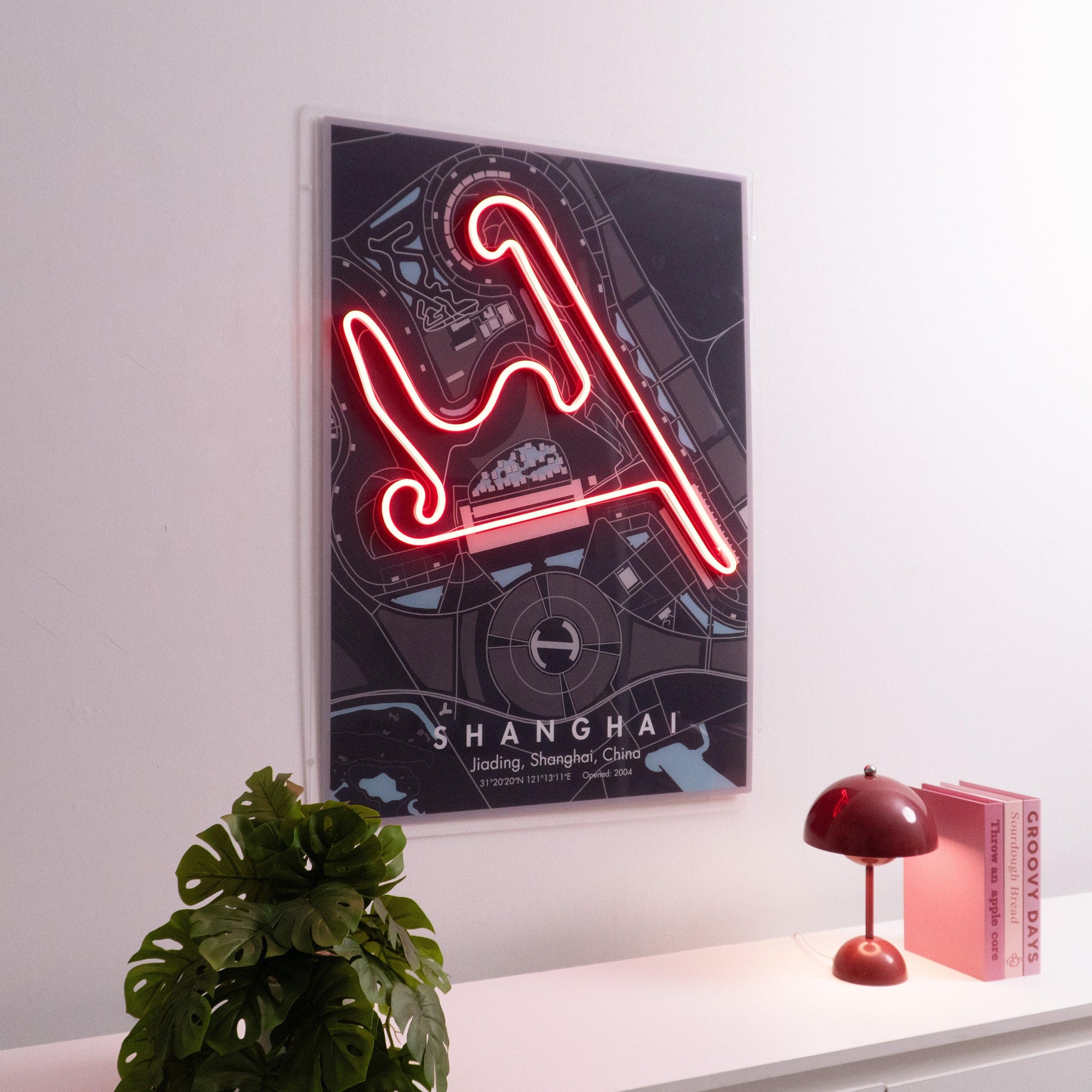 Interior wall with neon-lit Shanghai race track art, modern red lamp, pink books, and green plant