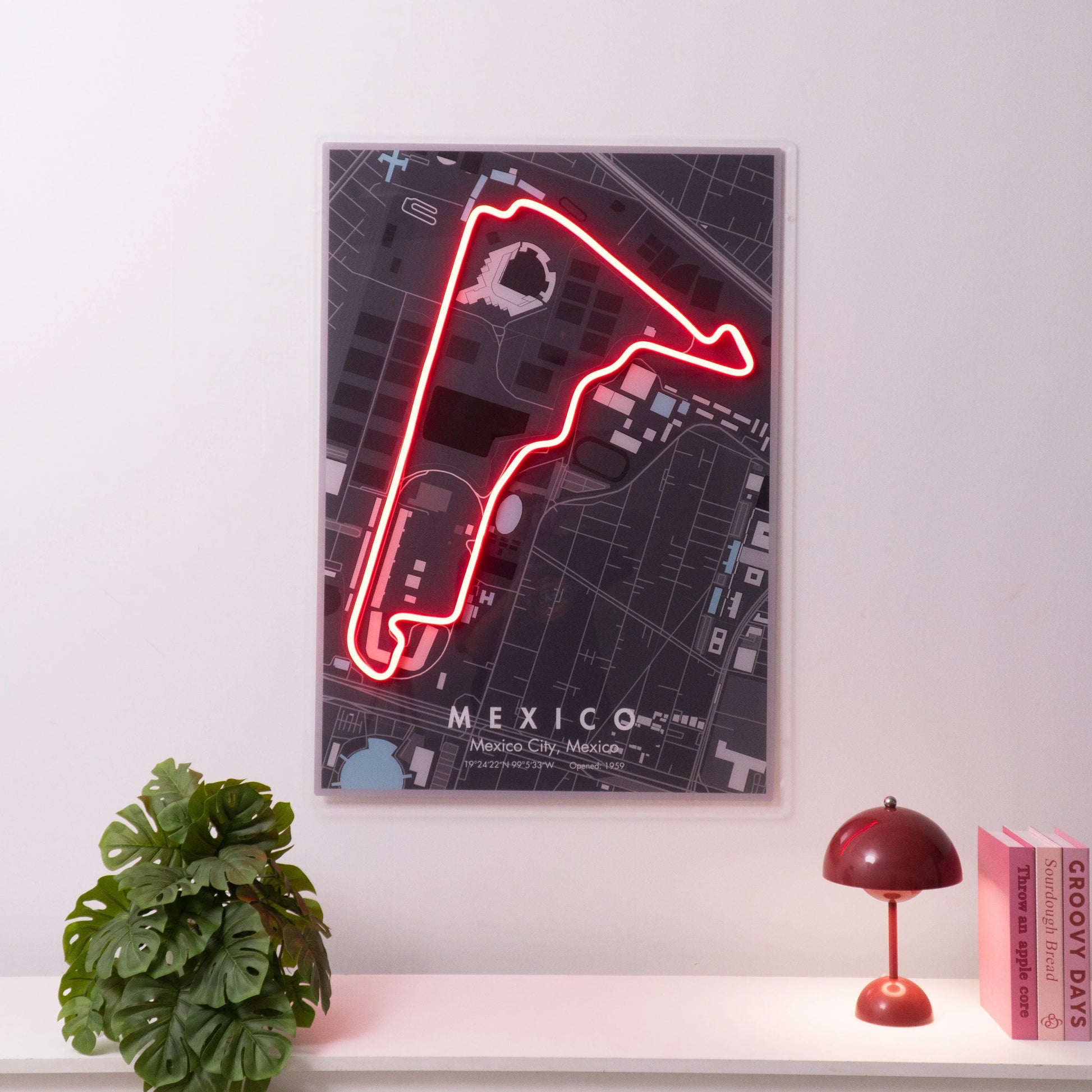 Neon-lit Mexico City race track map wall art above white shelf with plant, red lamp, and pink books
