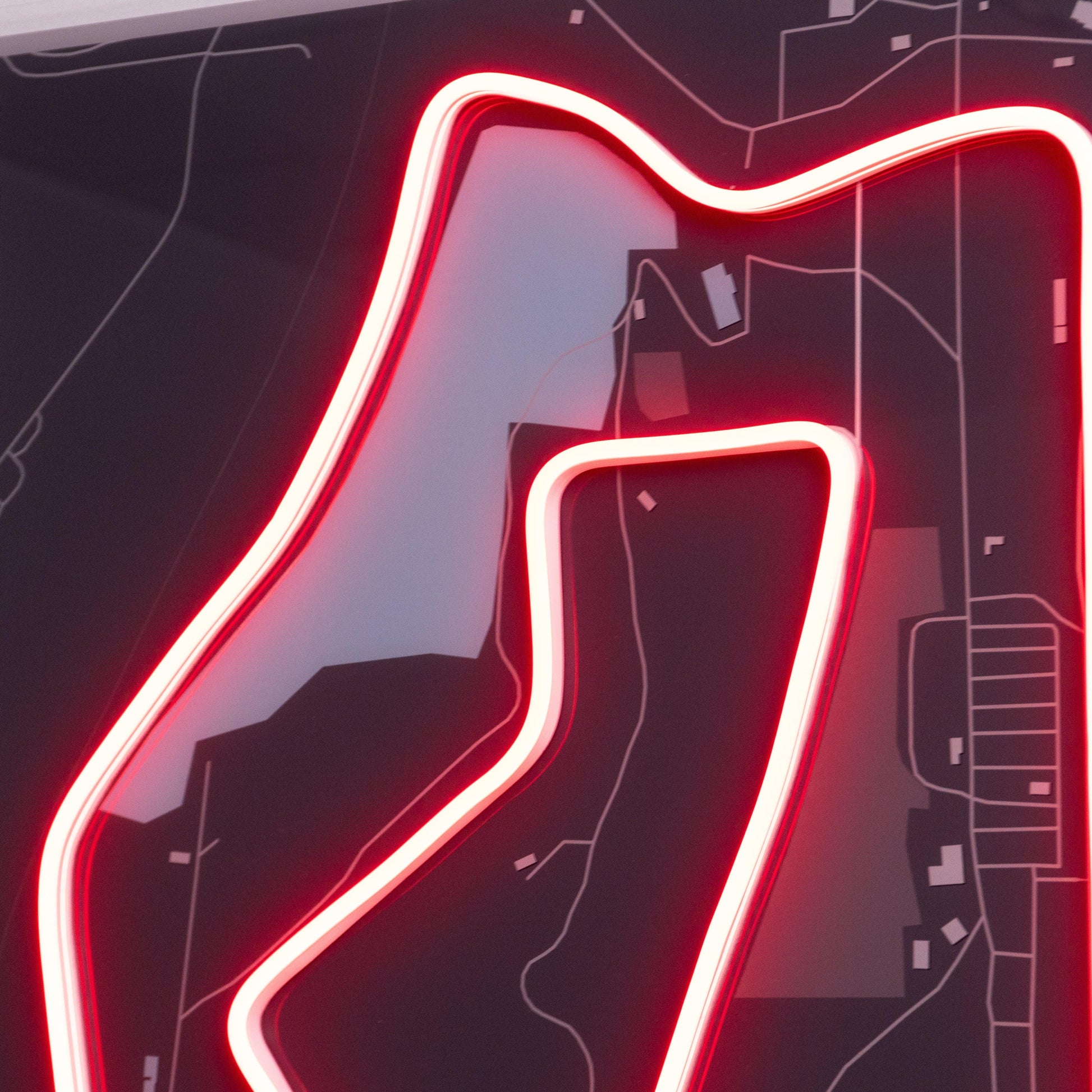 Close-up of a neon-lit map highlighting a winding road or race track in red with surrounding dark streets and buildings