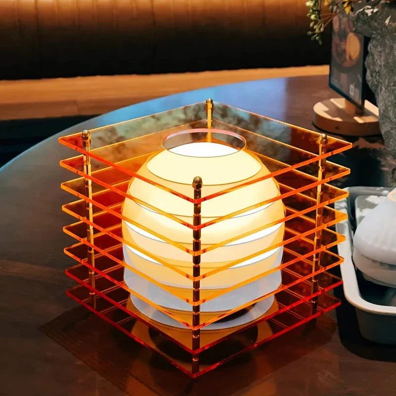 Modern spherical table lamp inside layered orange acrylic cage on wooden table