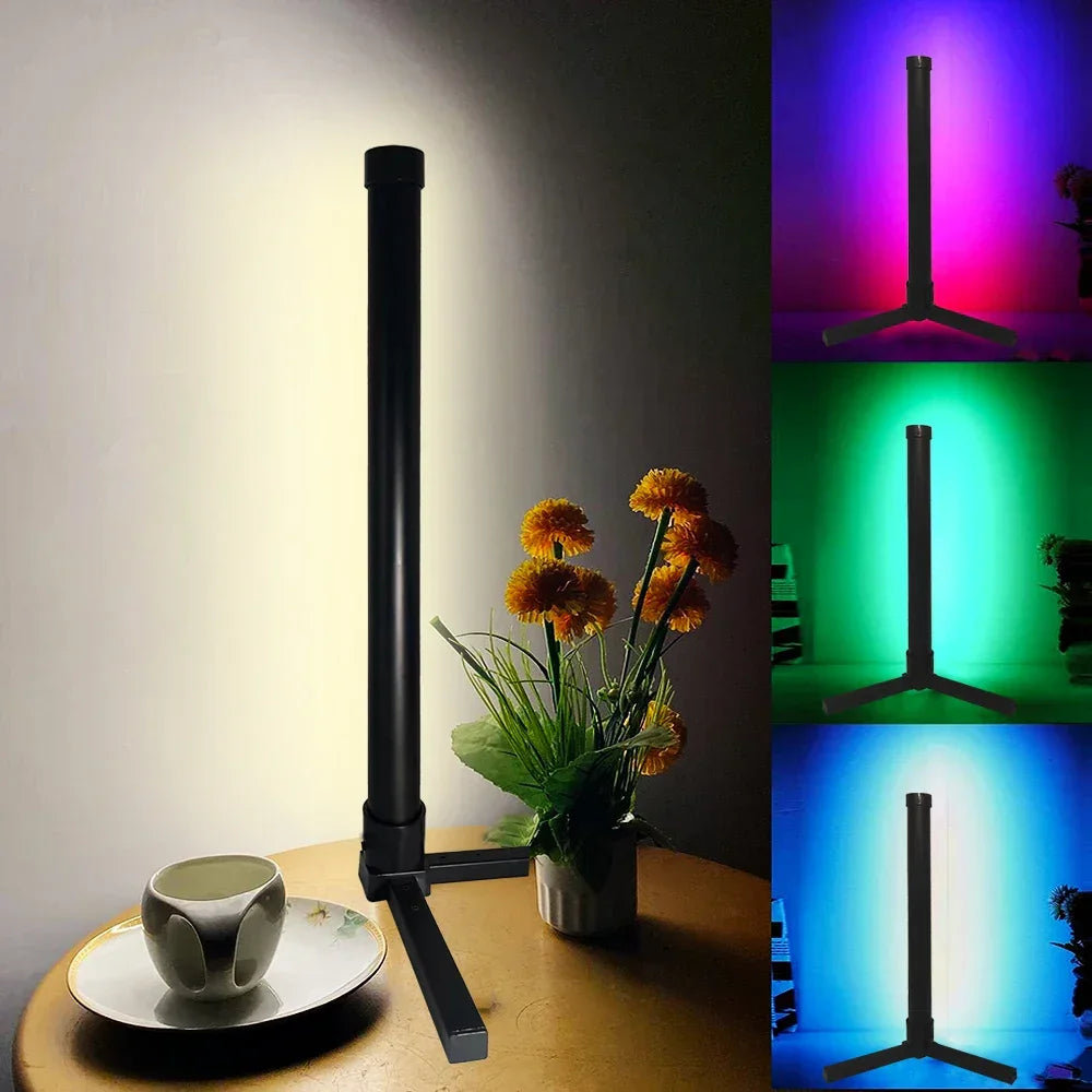 Modern black tripod lamp on a table with colorful background lighting and yellow flowers
